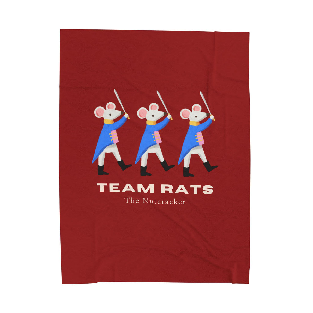 A red rectangular fabric item, likely a towel or blanket, featuring a graphic of three cartoon rats dressed as Nutcracker soldiers with swords, above the text 'TEAM RATS' and 'The Nutacker'.