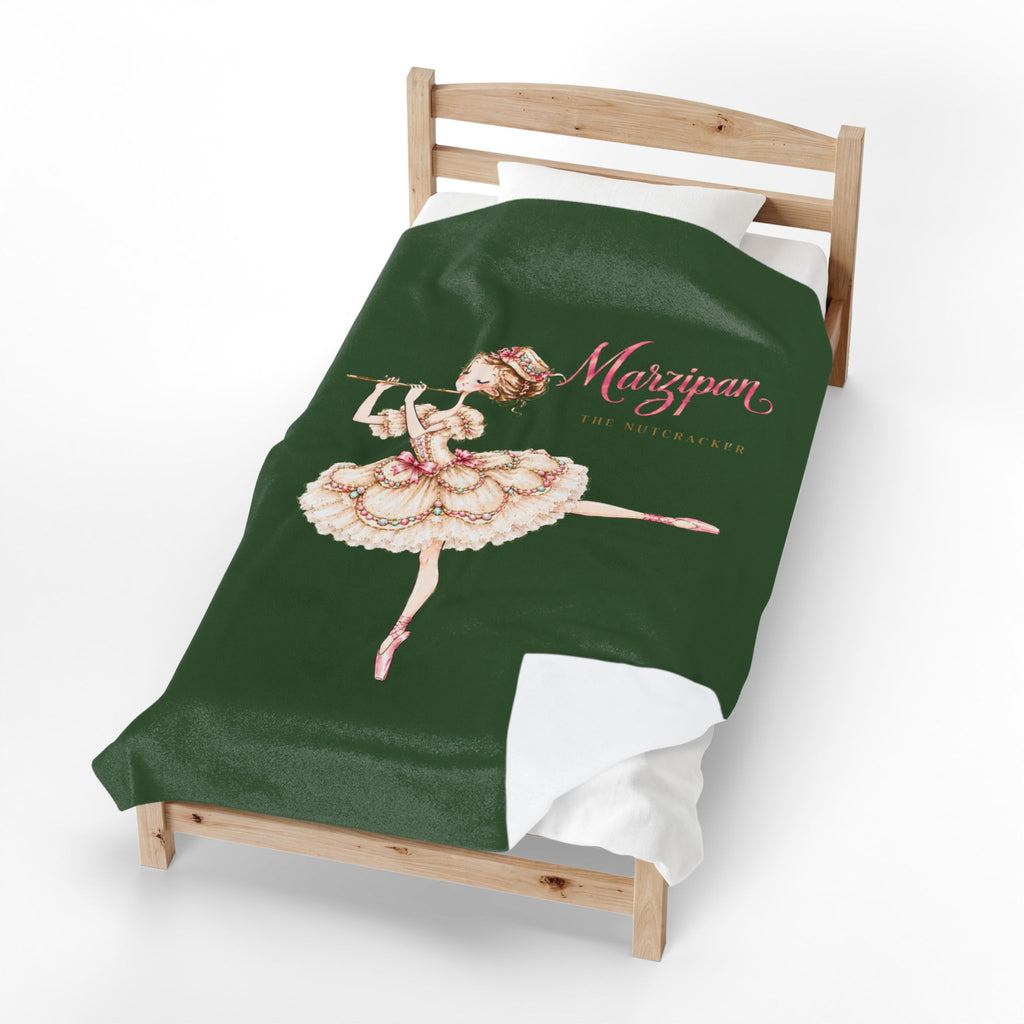 A dark green toddler bed blanket featuring a vintage-style ballerina illustration and the text 'Marzipan' and 'Toy Maker', displayed on a wooden bed frame against a white background.