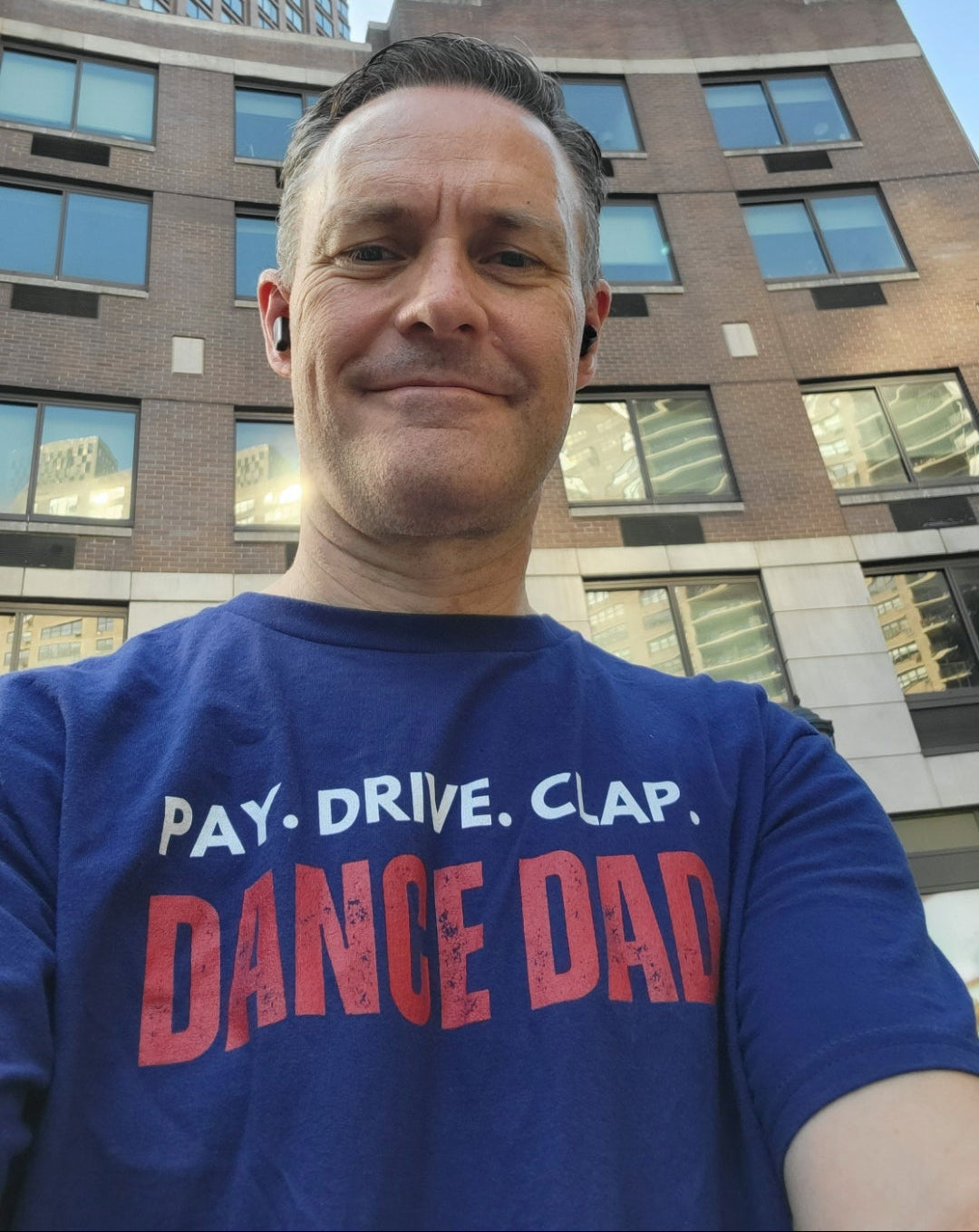 Man wearing a blue t-shirt with text standing in front of a building