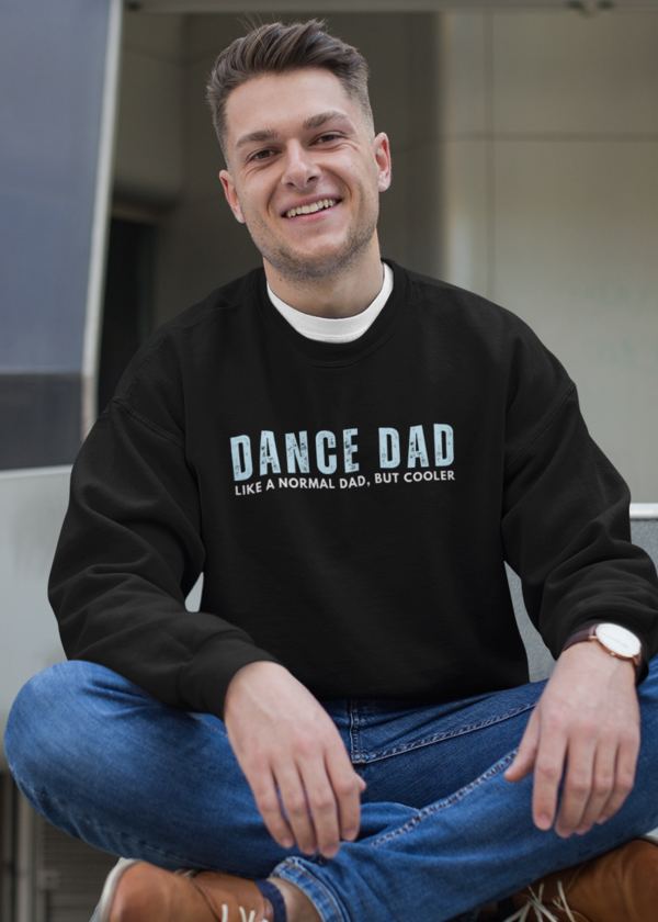 Man wearing a black sweatshirt with 'DANCE DAD' text, sitting on a step.