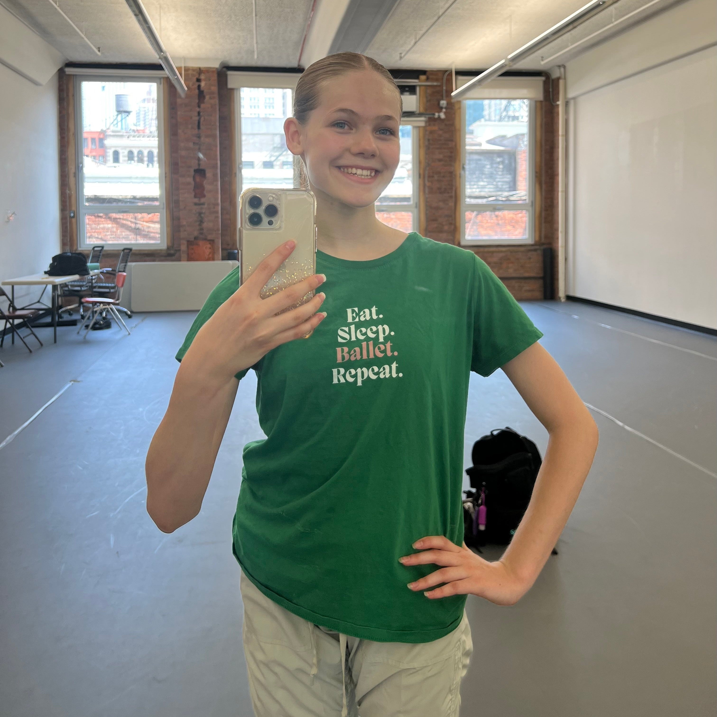 Person taking a mirror selfie in a room with large windows and a whiteboard.