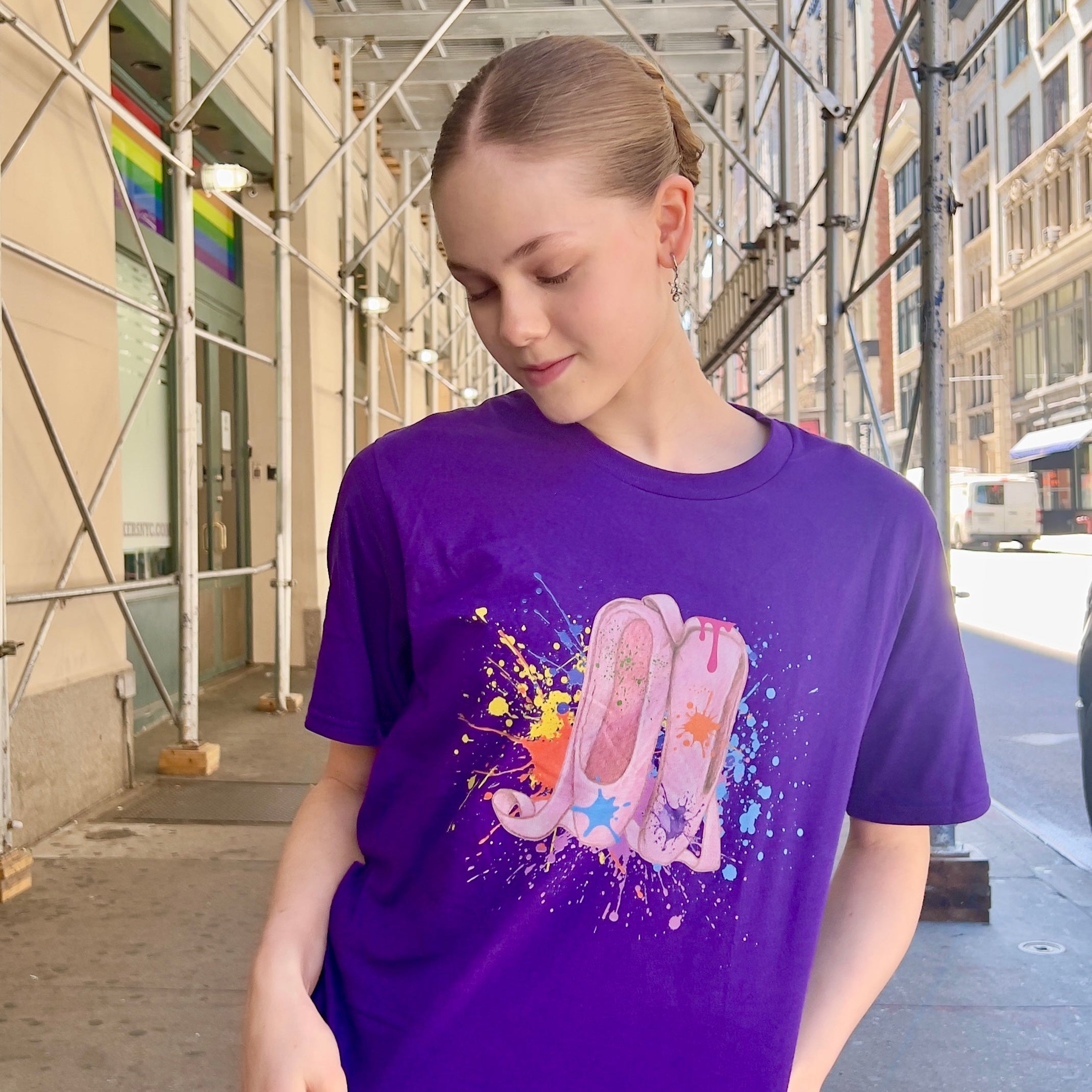 Person wearing a purple t-shirt with a colorful graphic on a city street.